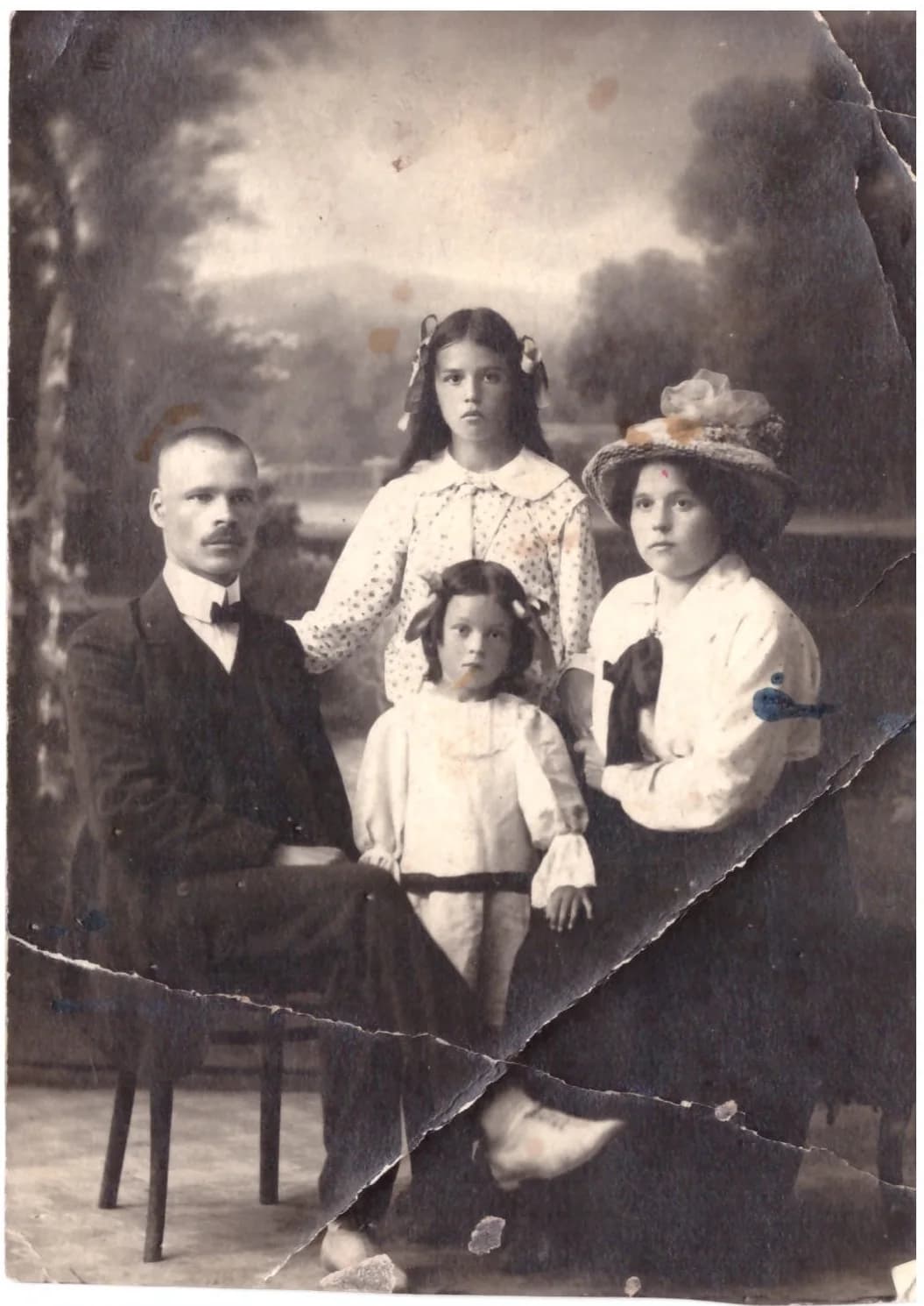 Старая семейная фотография в ателье: диагональный разлом через кадр, выпавшие куски бумаги внизу, синие и рыжие пятна